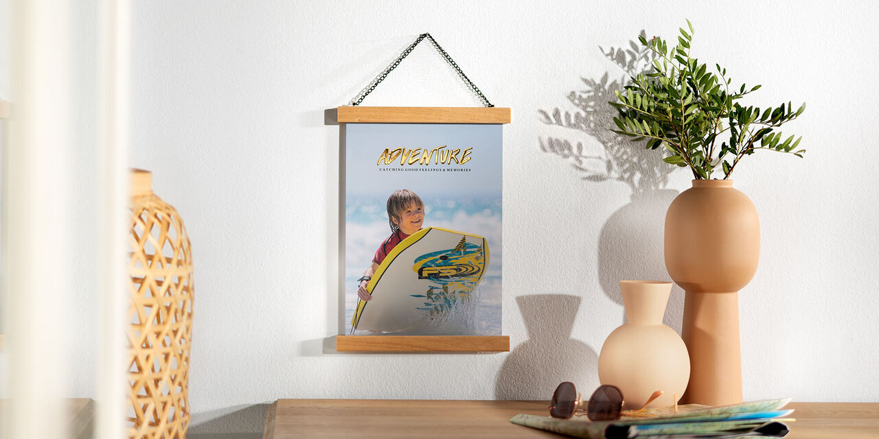 Dieses Poster zeigt einen kleinen Jungen am Strand. Er schaut in Richtung der Kamera und hält ein Surfbrett fest. Im Hintergrund sieht man das Meer und seine Wellen. Darüber ist der blaue Himmel zu erkennen.